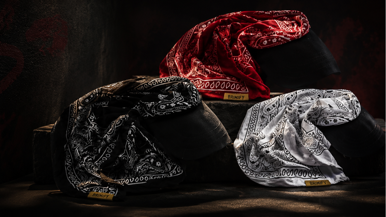 A dark promotional banner for Brimify The Brimuna statement headwear, showing three sculptural bucket-style caps in black, red, and silver on a dark background with large text reading 'TOP IT OFF. TIE IT DOWN.